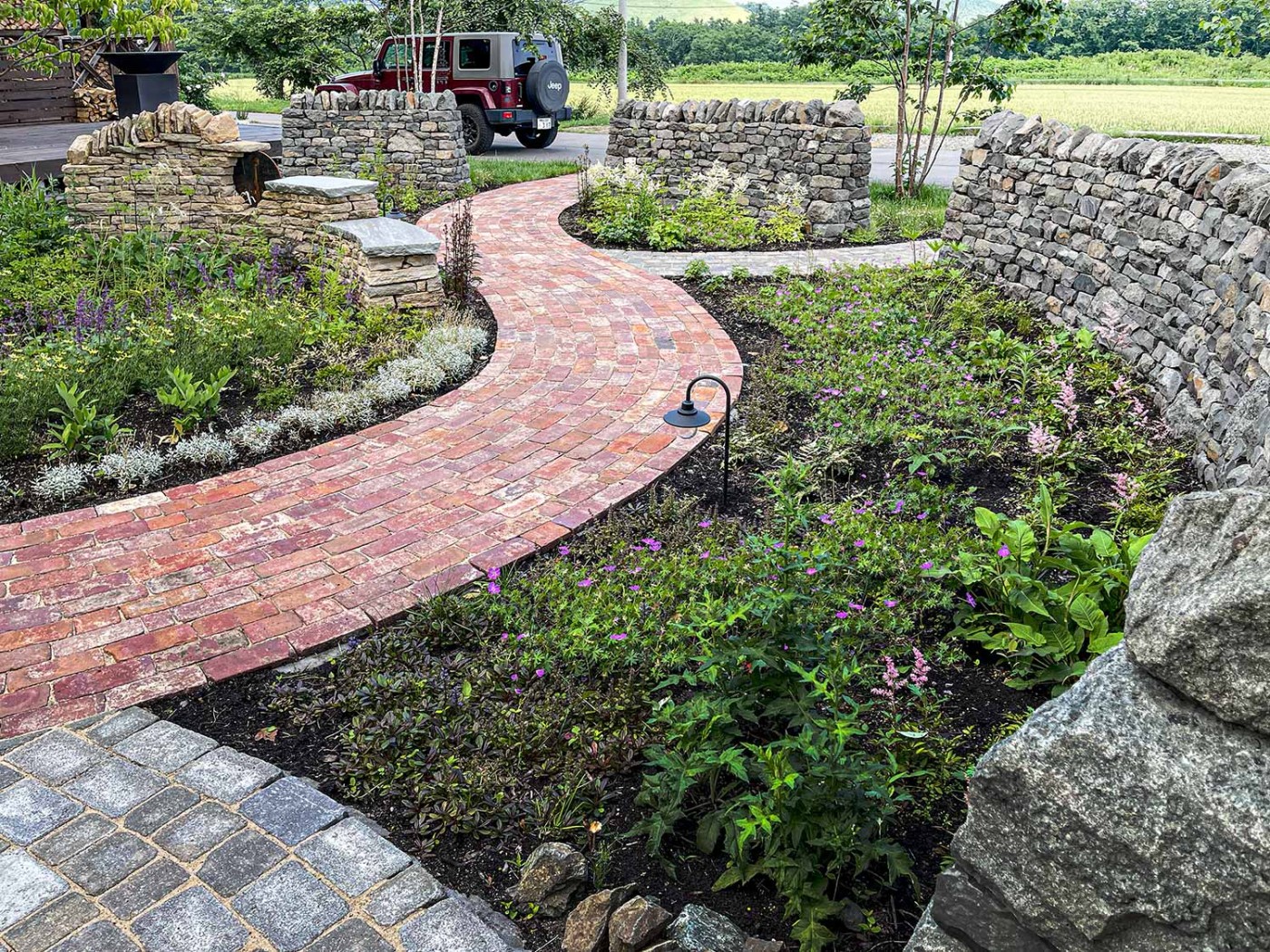 曲線のアプローチは視点の変化による効果で狭いお庭でも多様な景色を感じさせてくれます。 宿根草は、その視点の変化に呼応するようにポイントを設けて色彩と高さに変化を持たせています。